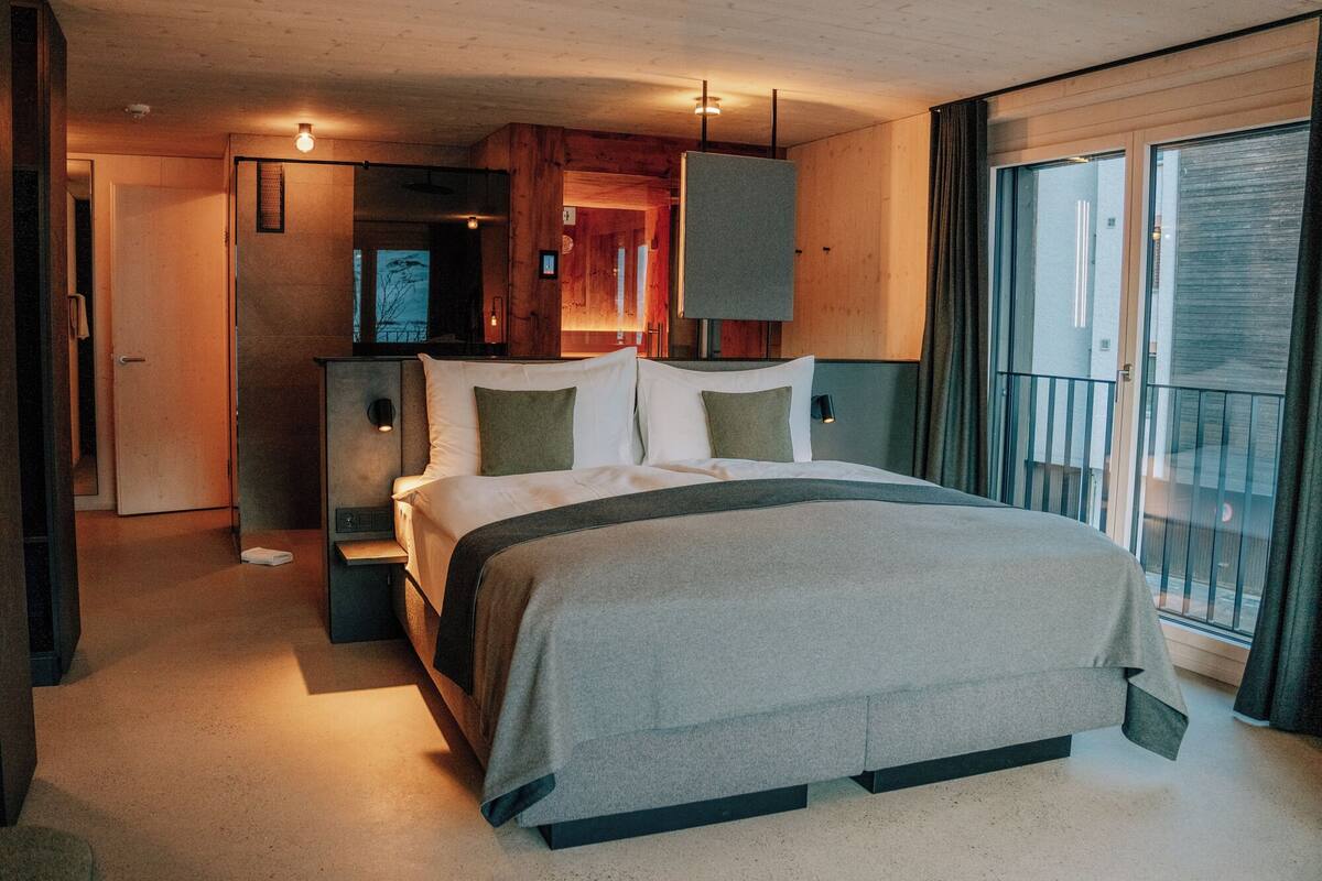 Ein modernes Schlafzimmer mit einem großen Bett, einem Nachttisch, einer Wandlampe und einer Schiebetür zum Außenbereich.