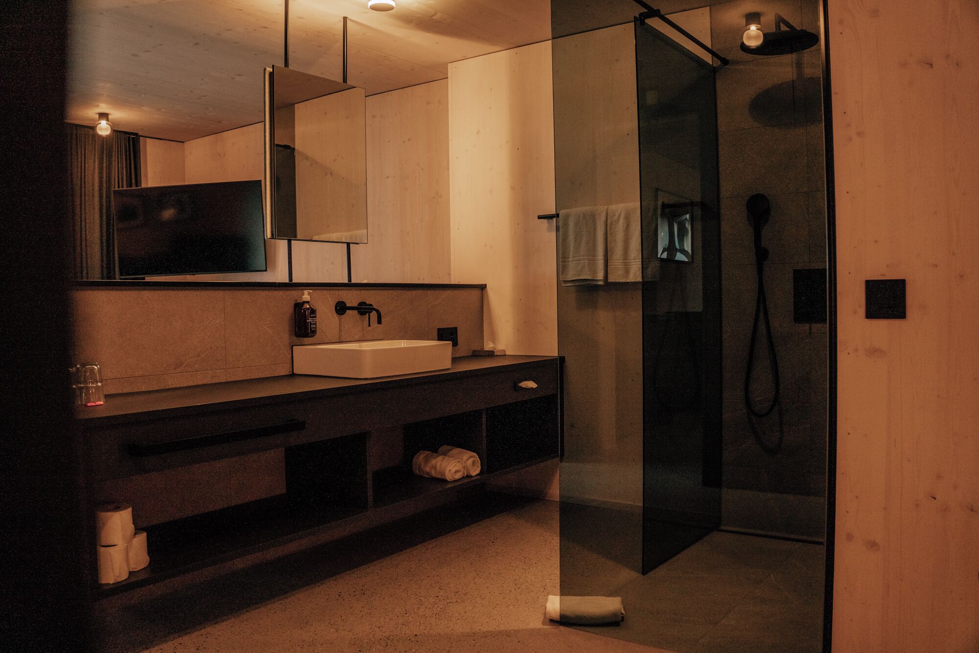 Un baño moderno con un espejo grande, un lavabo y una zona de ducha con mampara de vidrio.