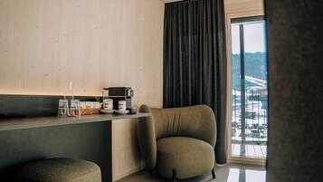 Een moderne kamer met een houten wand, een donker gordijn, een koffieapparaat en uitzicht op een besneeerd landschap door een groot raam.