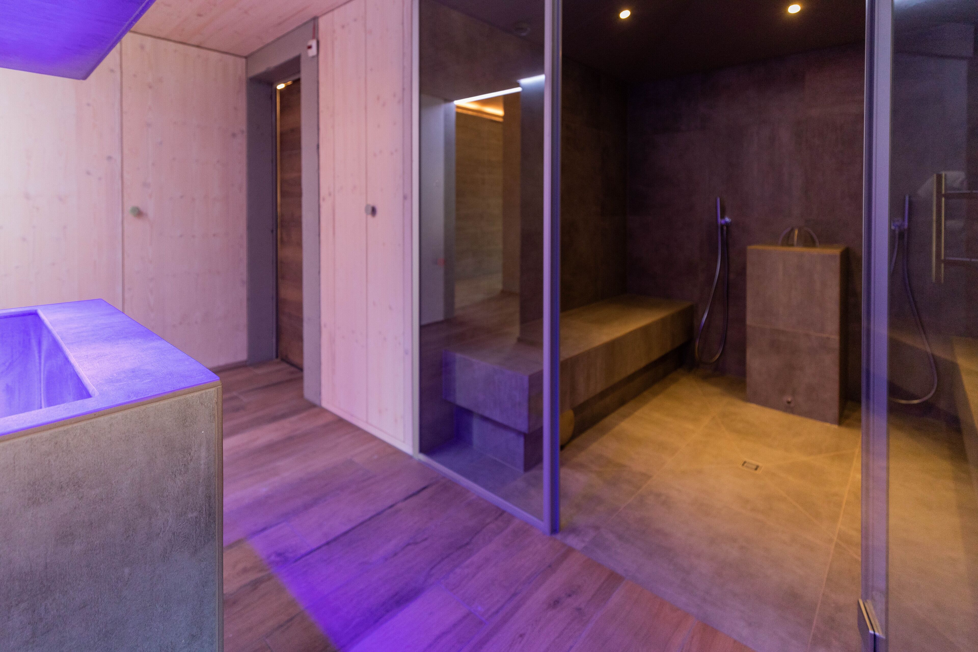 Une salle de bain moderne avec un plancher en bois, une douche en verre et un banc en béton.