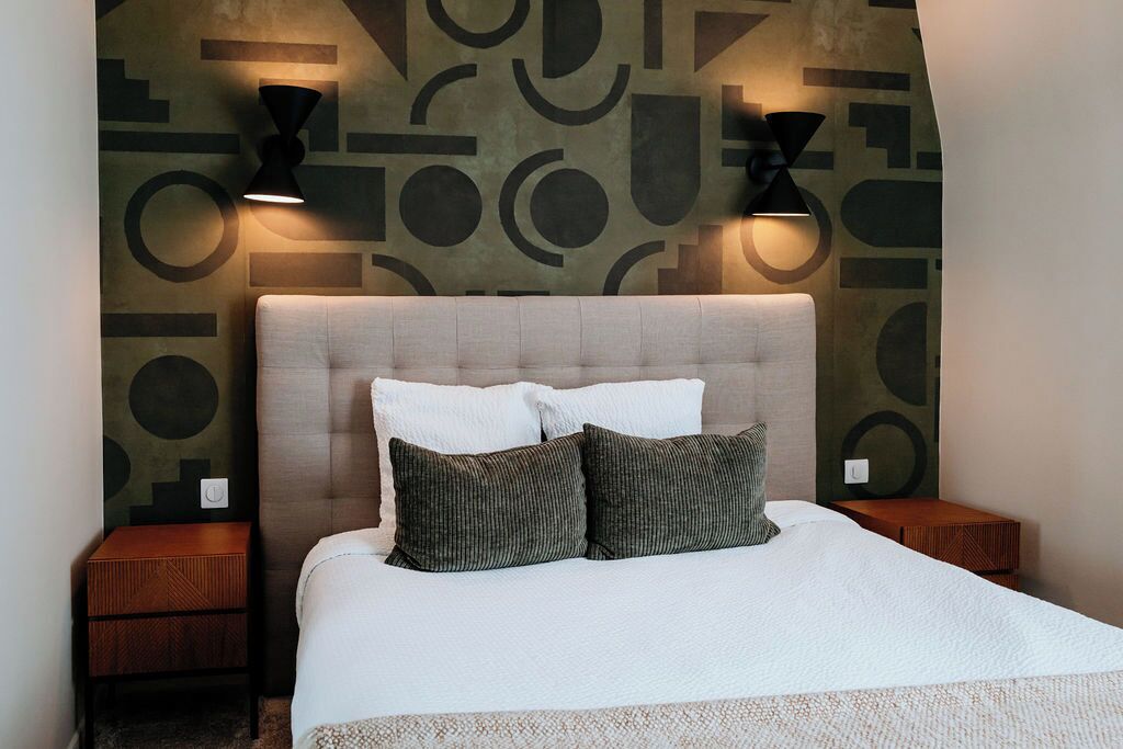A neatly made bed with two pillows, a headboard, and two bedside tables with lamps.