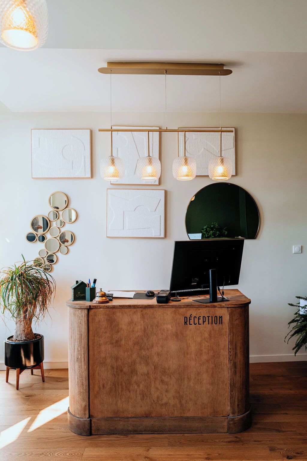 A reception desk with a wooden finish and the word "RECEPTION" on it. Above the desk, there are framed artworks and pendant lights.