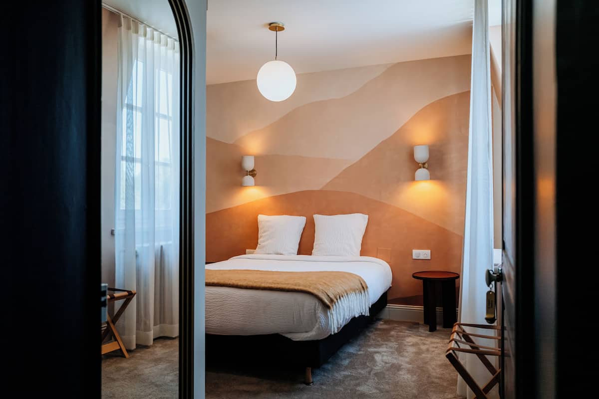 A bedroom with a bed, bedside lamps, a round ceiling light, and a view through an open door.