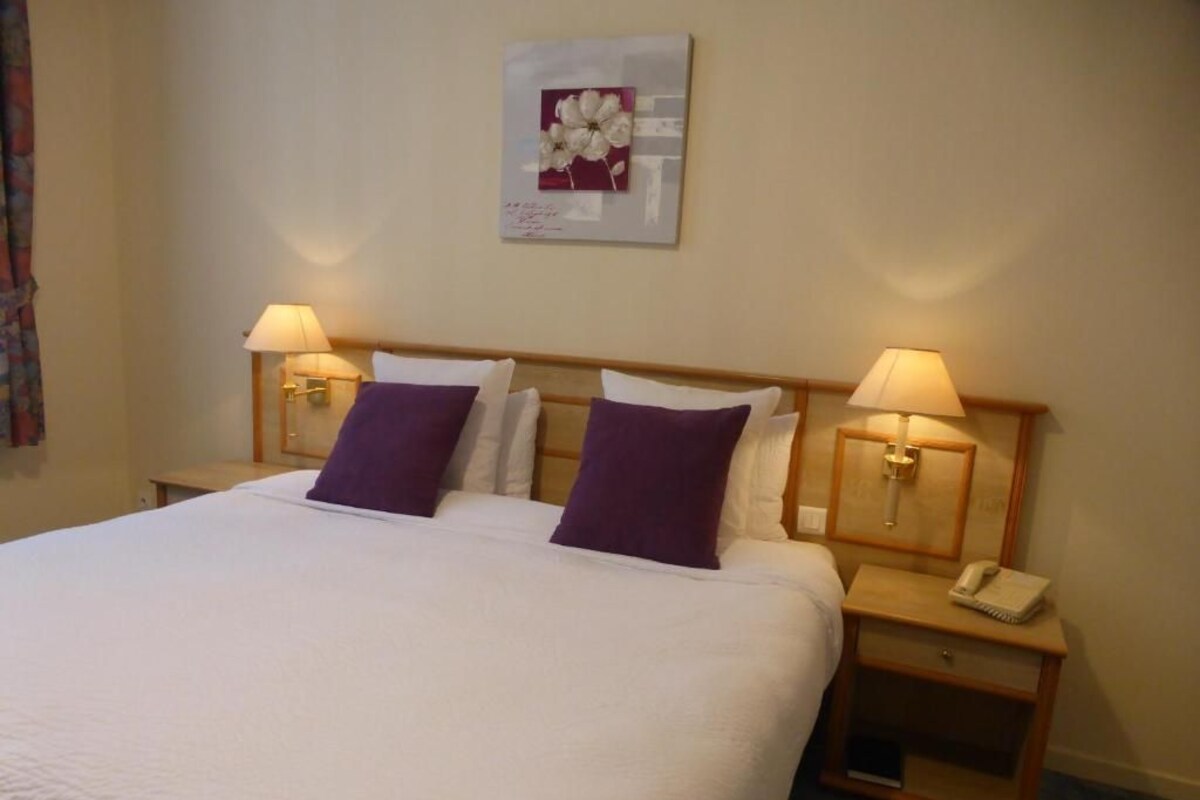 A hotel room with a large bed, two bedside lamps, a nightstand with a phone, and a framed picture on the wall.