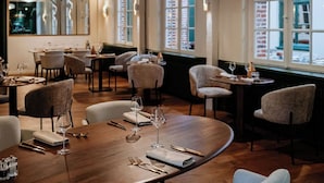 Interior moderno de restaurante con mesas de madera, sillas tapizadas y grandes ventanales con vistas a la ciudad.