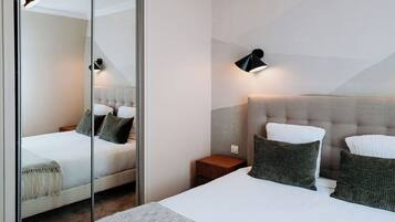 Un dormitorio moderno con una cama grande, una mesita de noche, un espejo y una lámpara de pared.