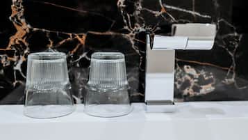 A bathroom with a marble backsplash, a white sink, and two clear glass cups.