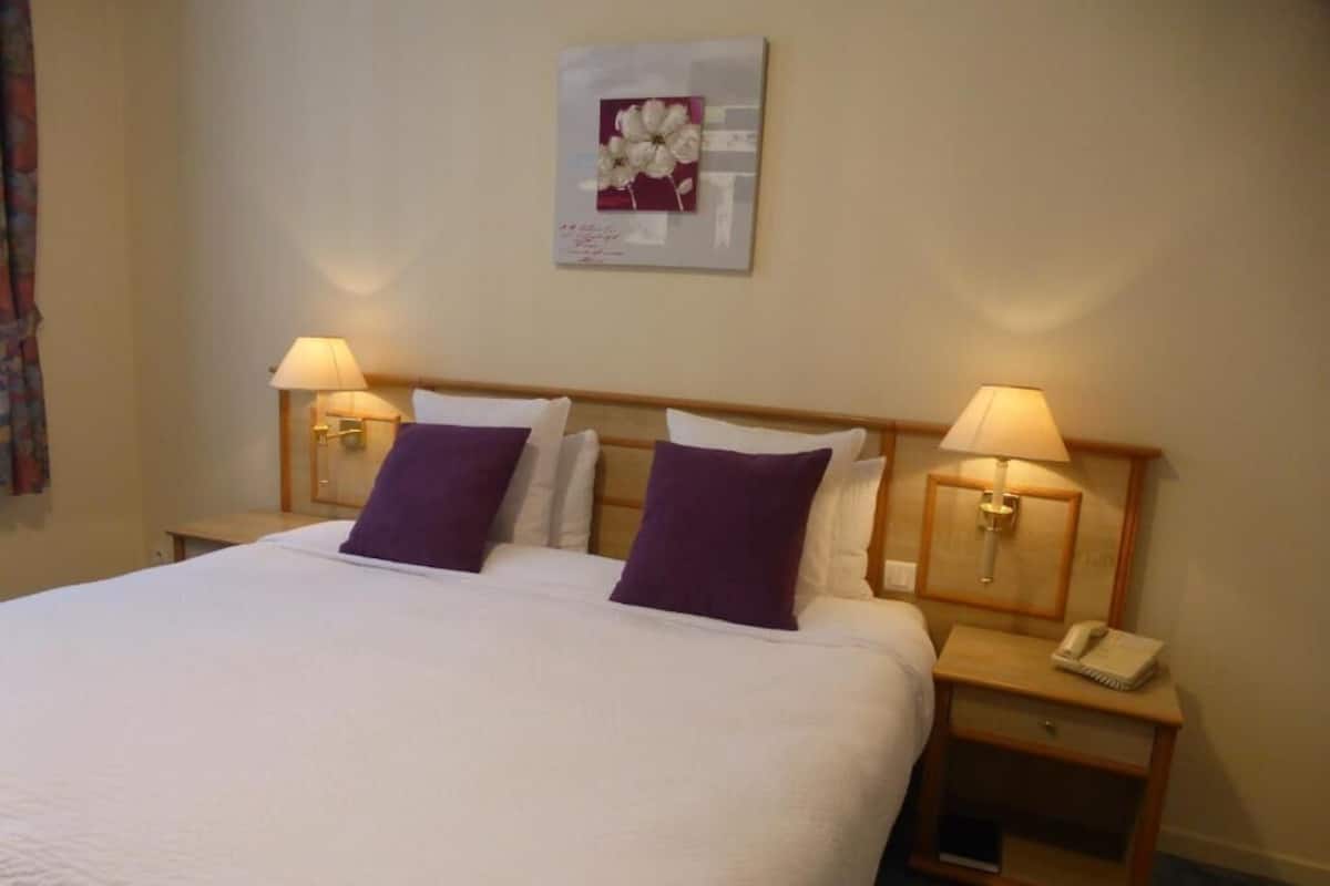 A hotel room with a large bed, two bedside lamps, a nightstand with a phone, and a framed picture on the wall.