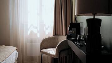 A hotel room with a bed, a desk with a lamp, a chair, and a television.