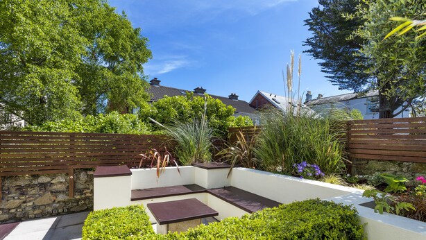 A garden patio with a stone wall, wooden fence, and various plants.