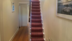 A hallway with a wooden floor, a red carpeted staircase, and a framed picture on the wall.