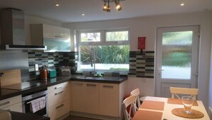 A modern kitchen with a window, a dining area with a table and chairs, and a view of greenery outside.