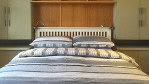A bedroom with a bed, two bedside lamps, a wooden headboard, and built-in shelving above the bed.