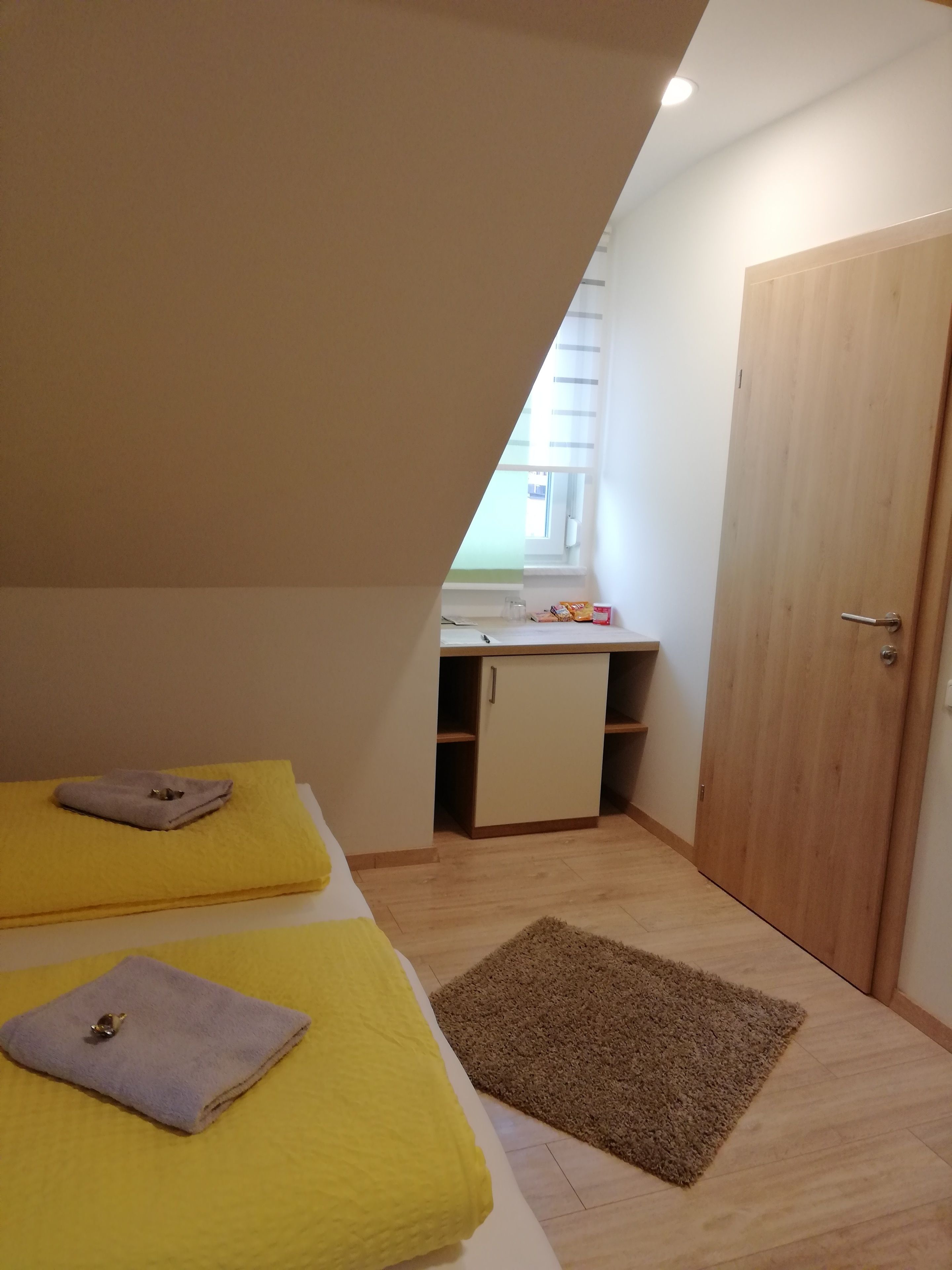 A small, triangular attic bedroom with two beds, a wooden door, and a kitchenette.