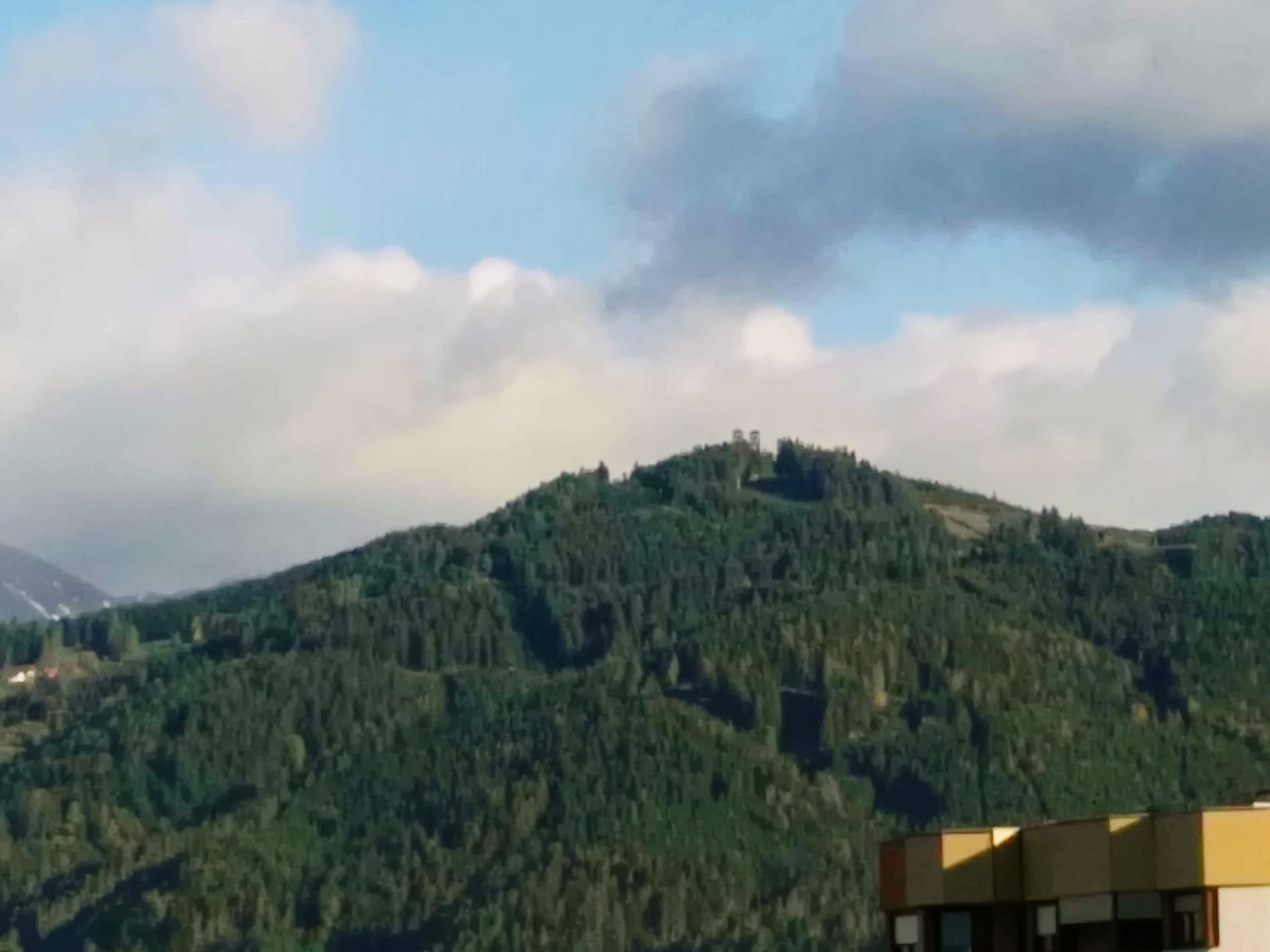 Een bergachtig landschap met een dicht bos en een gebouw met moderne architectuur op de voorgrond.