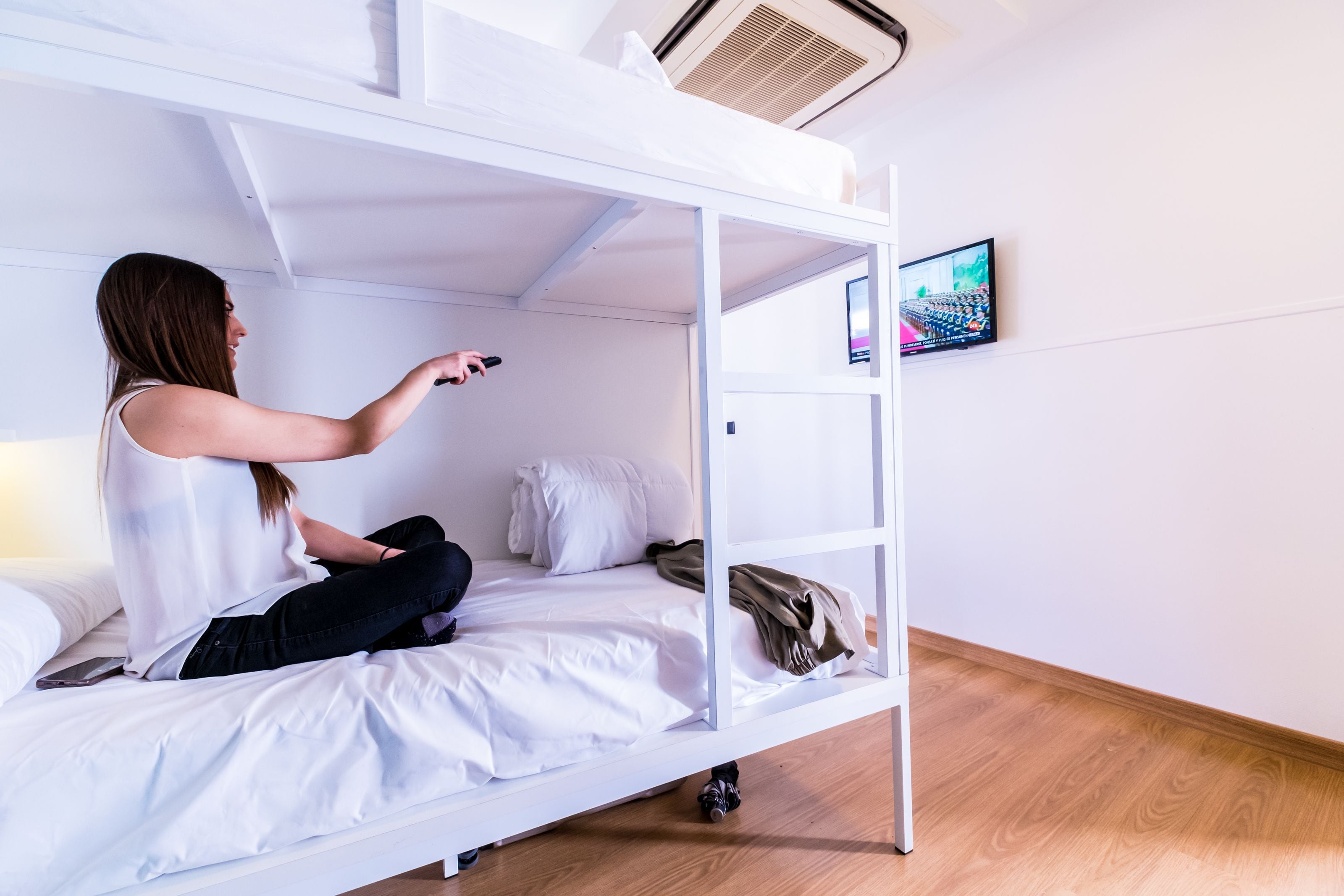 A bunk bed with a TV mounted on the wall, a smartphone on the bed, and a pair of shoes on the floor.