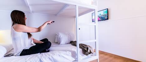 A bunk bed with a TV mounted on the wall, a smartphone on the bed, and a pair of shoes on the floor.