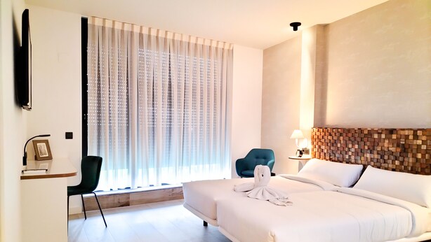 A hotel room with a bed, a desk, a chair, a TV, and a window with curtains. - Far Home Bernabeu (Madrid)