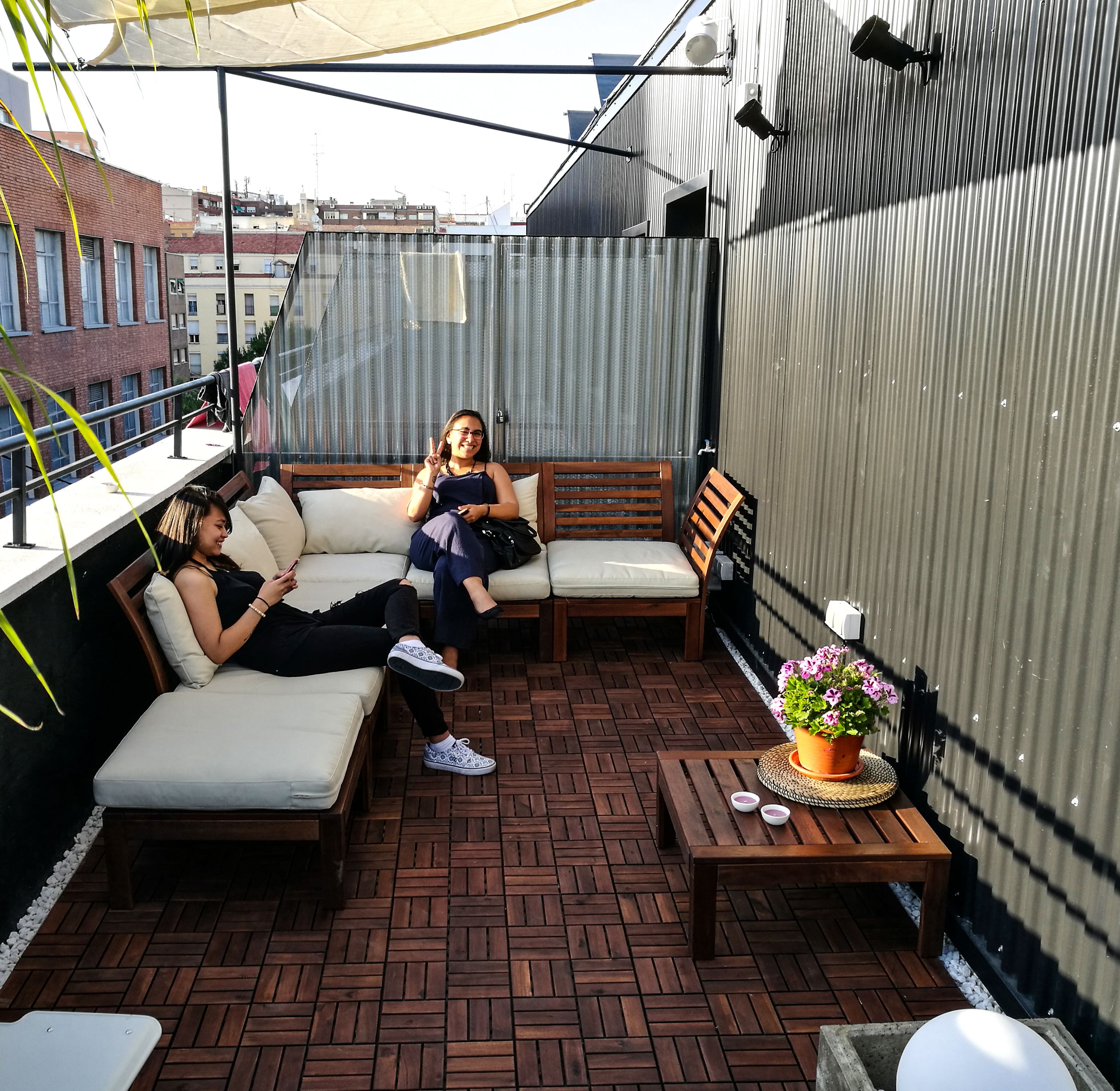 Un espacio al aire libre con una banca de madera, un sofá acolchado y una pequeña mesa con una planta en maceta.