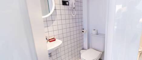 A modern bathroom with a white toilet, a sink with a red soap dispenser, and a hairdryer mounted on the wall.