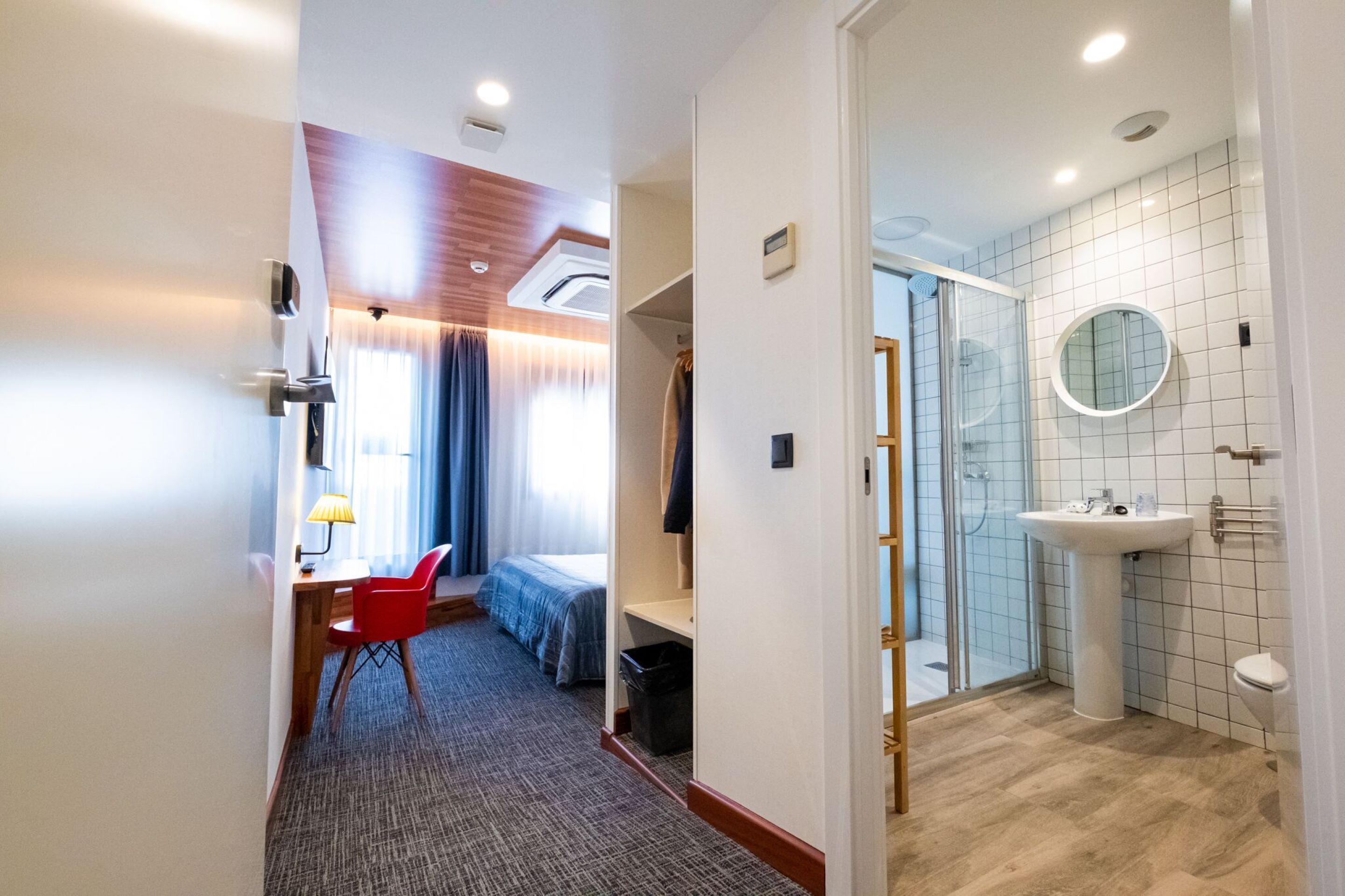 Una habitación de hotel con cama, escritorio, silla y baño con lavabo y ducha.