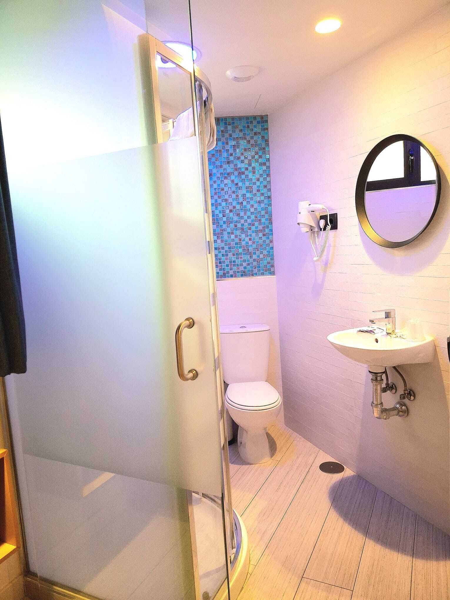 A bathroom with a glass shower enclosure, a toilet, a sink, and a mirror.