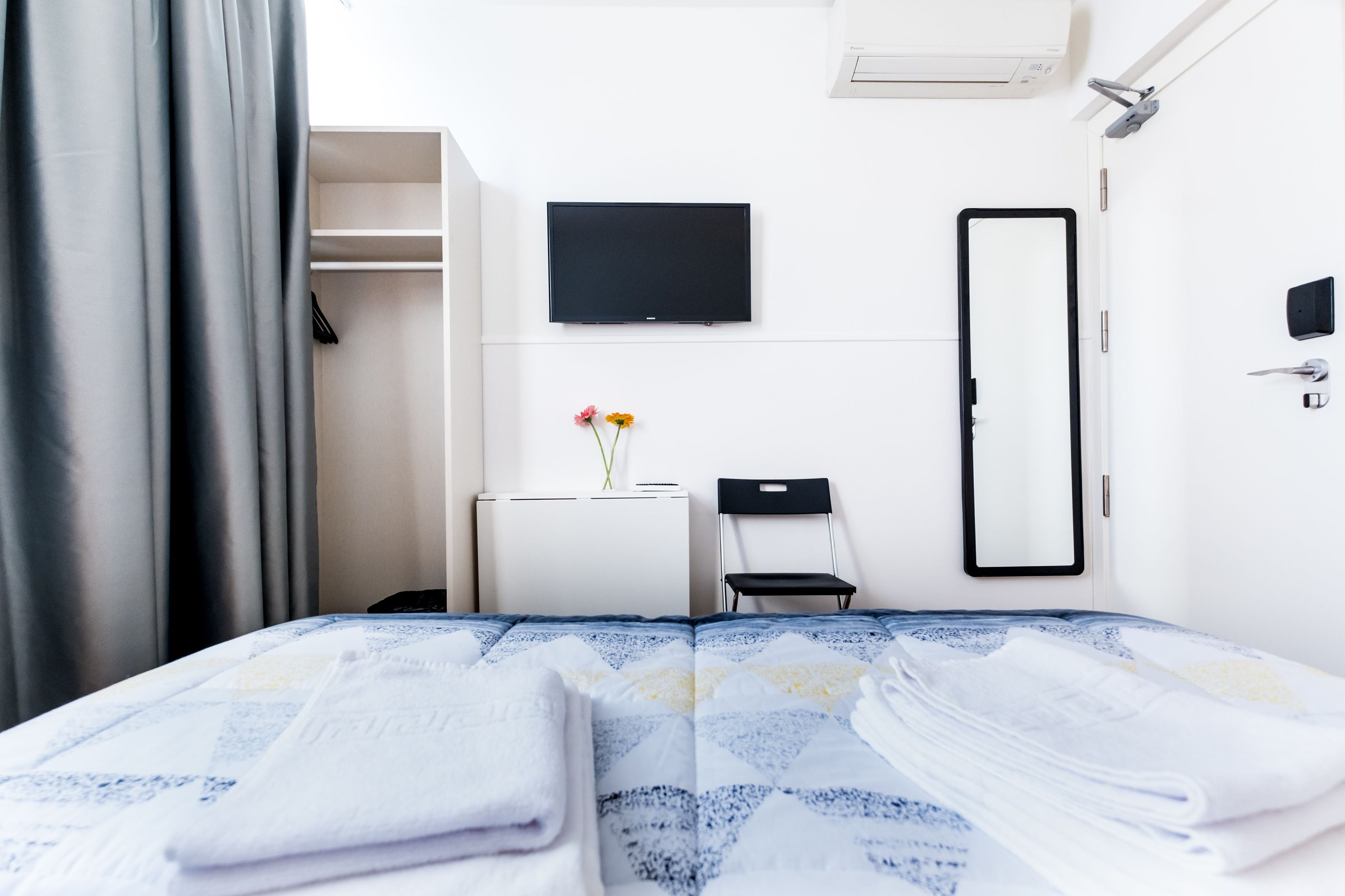 A hotel room with a bed, a desk, a chair, a TV, a mirror, and a wardrobe.
