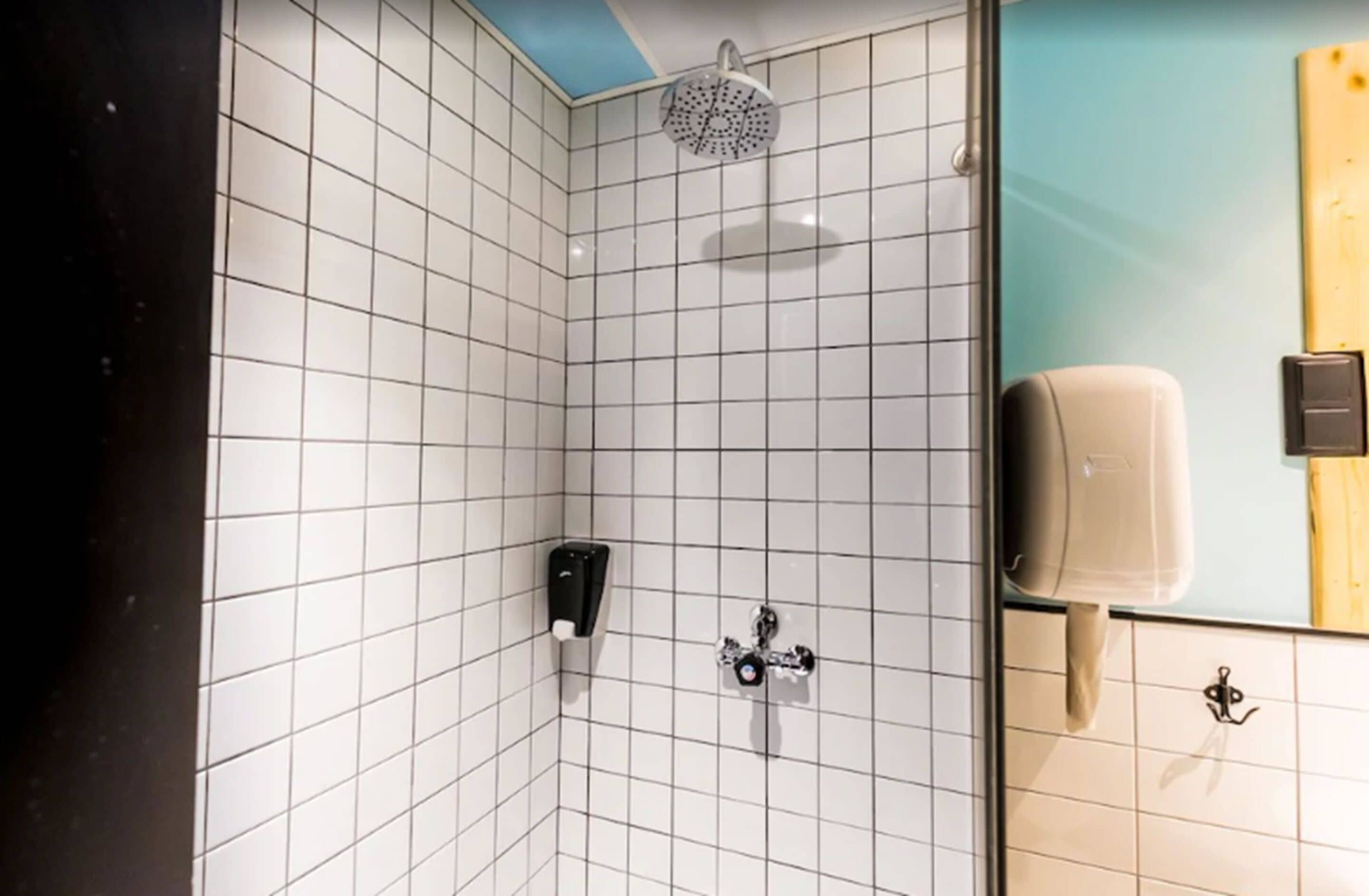 A bathroom with white tiled walls, a shower with a circular head, a soap dispenser, and a towel rack.