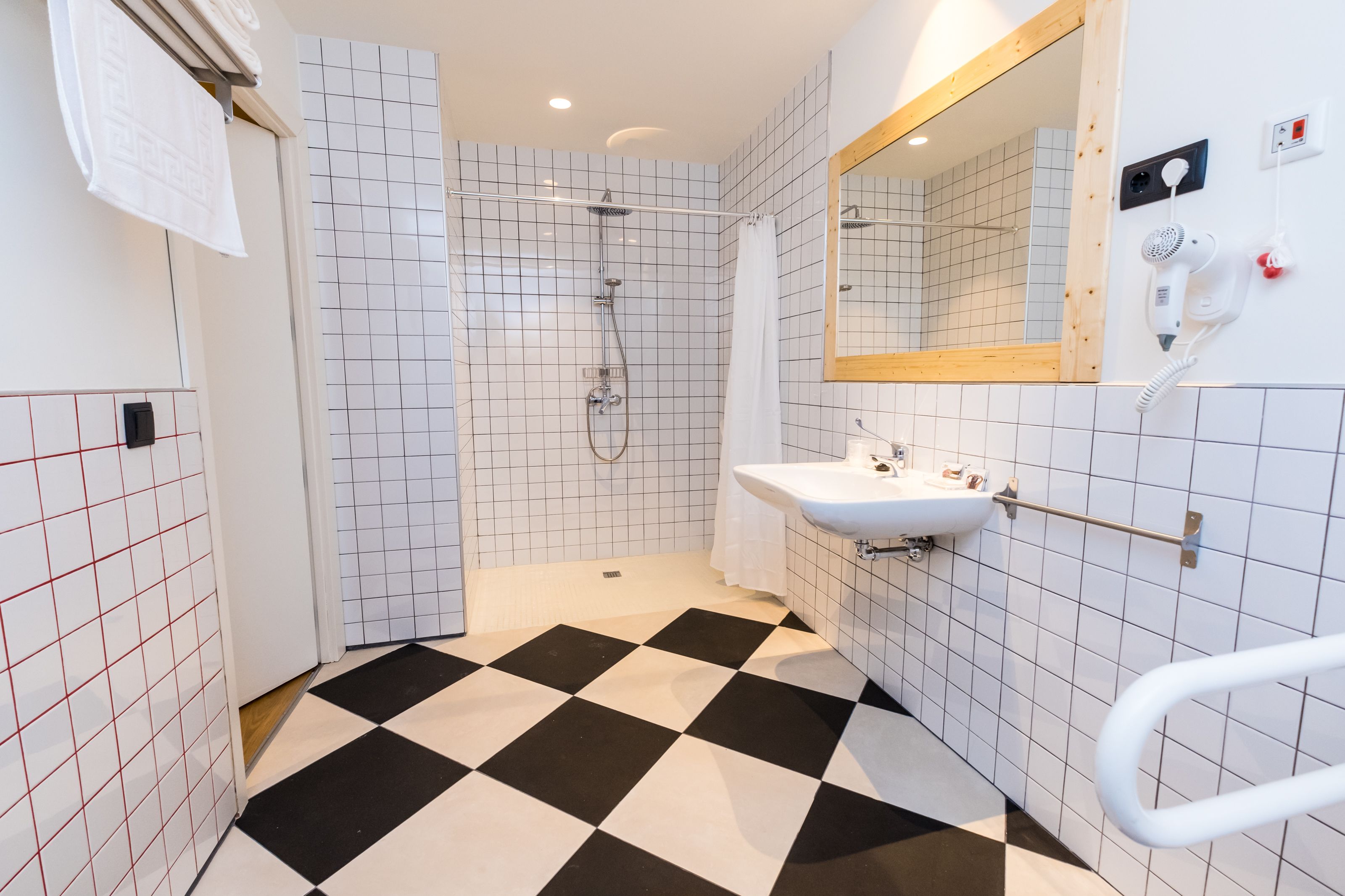 A bathroom with a shower, a sink, a mirror, and a hand dryer.