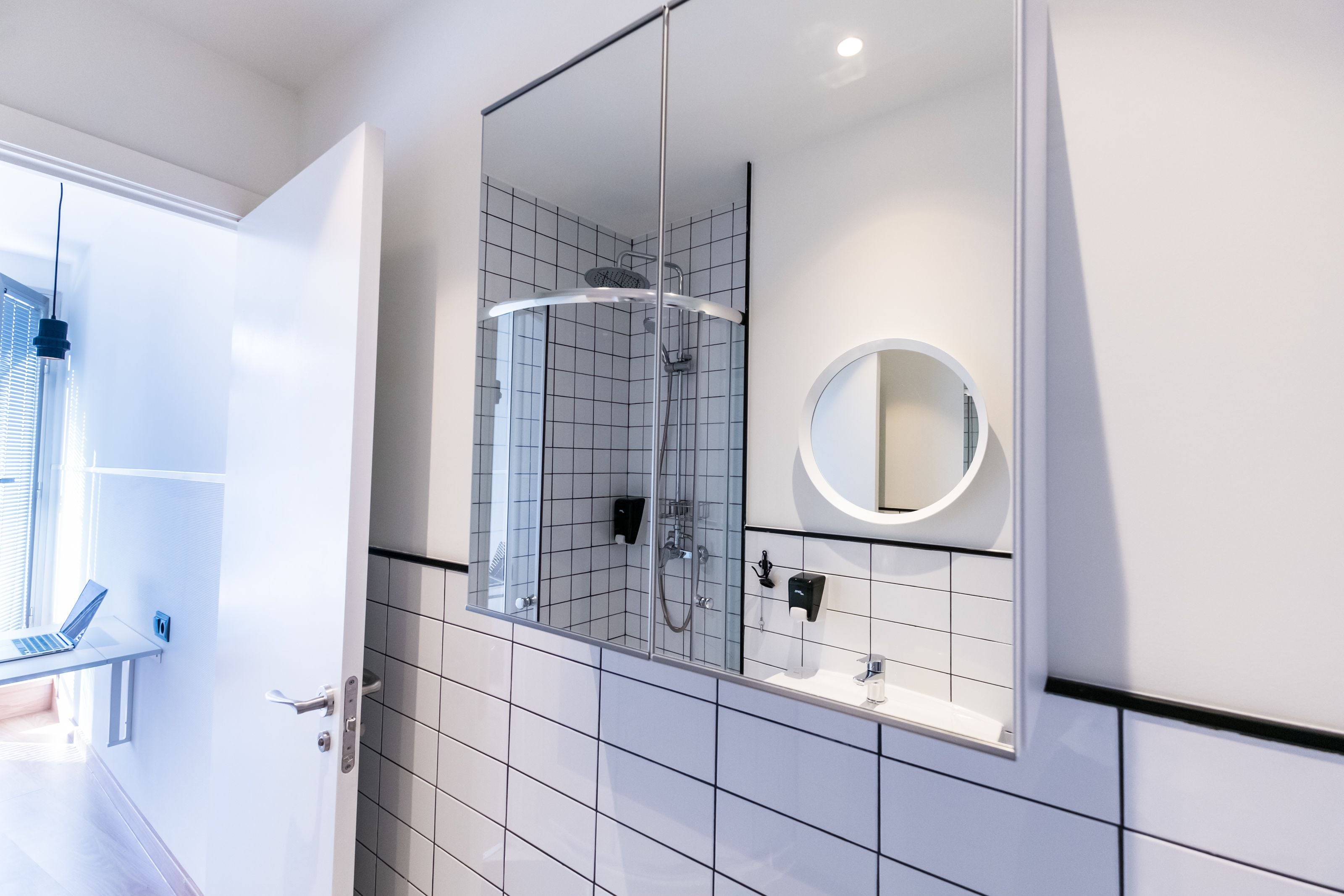 Un baño moderno con ducha de vidrio, un espejo redondo y pared de azulejos blancos.
