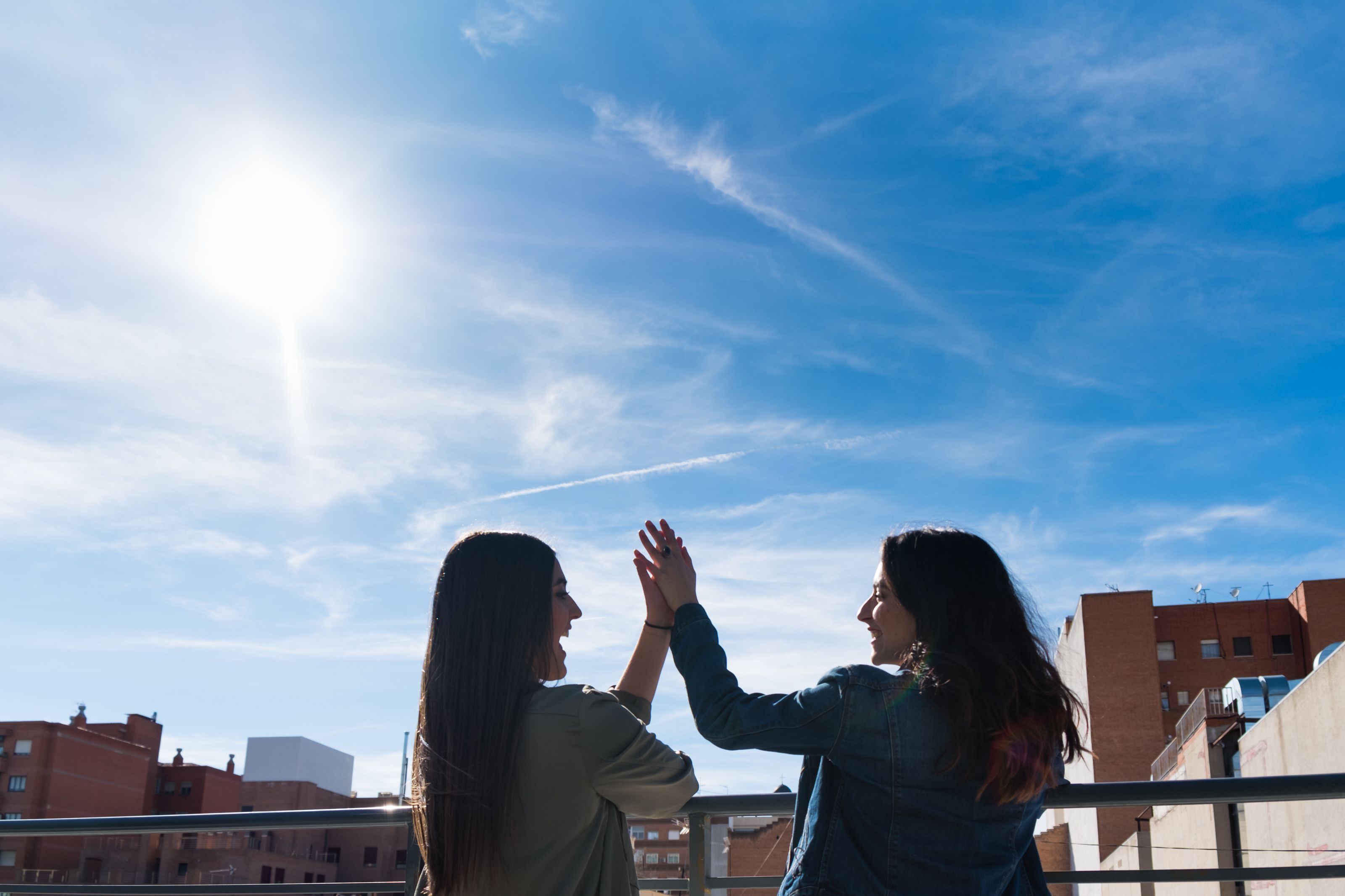 Dos personas chocando los cinco en una azotea, con cielo despejado y edificios al fondo.