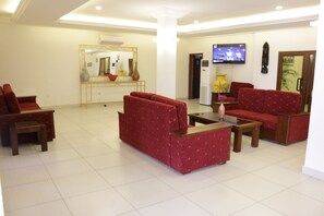 Un hall d’hôtel avec des canapés rouges, une table basse, un téléviseur et un comptoir de réception.