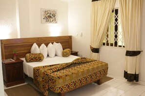 Une chambre à coucher avec une tête de lit en bois, une couvre-lit à motifs, une table de chevet avec un vase et une fenêtre avec des rideaux.