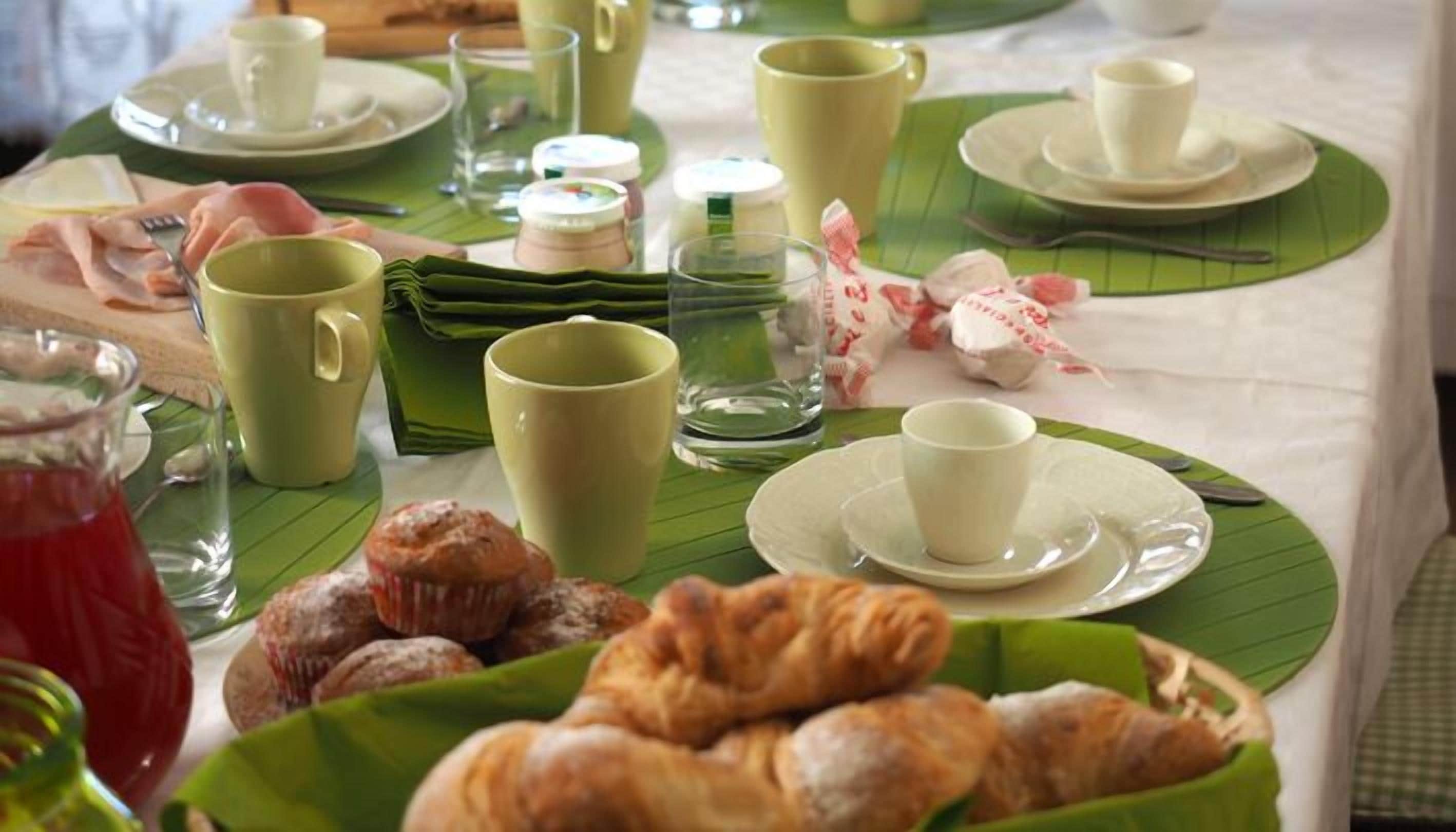 A breakfast setting with a table covered in a white tablecloth, featuring green leaf placemats, a variety of pastries, and several cups and glasses.