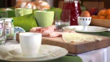 A breakfast table with various food items, including sliced cheese, ham, and eggs, along with condiments and beverages.