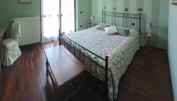 A bedroom with a wooden bed, a bedside table, a chair, and a window with curtains. - Ca' Rosa Bed & Breakfast (Malnate)