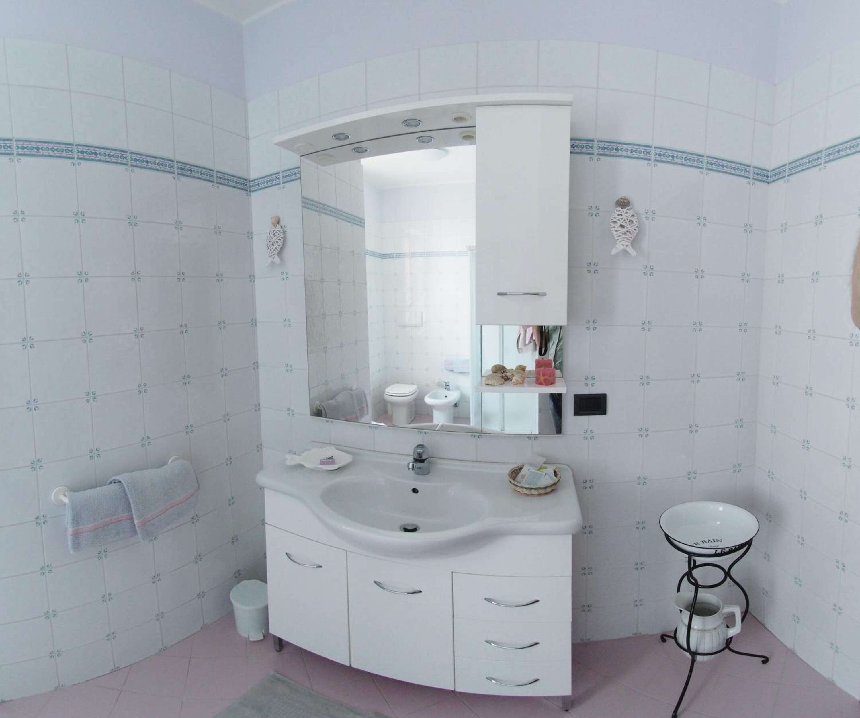 A bathroom with a white sink, a mirror, a toilet, and a small table with a cup.