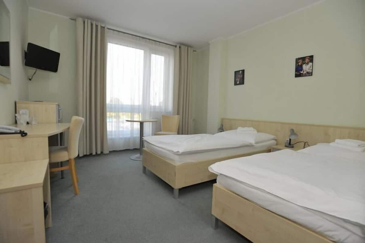 A hotel room with two beds, a desk, a chair, a TV, and a window with curtains.