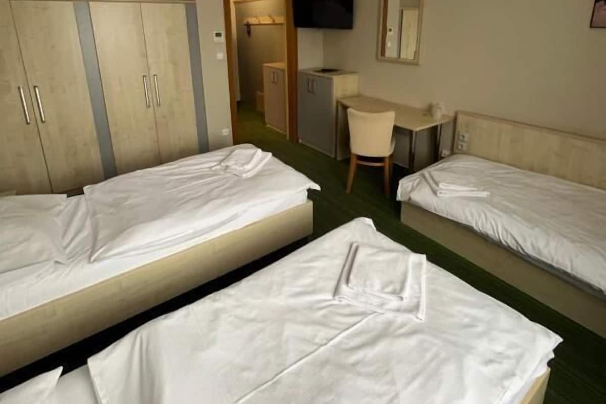 A hotel room with two single beds, a desk with a chair, a TV mounted on the wall, and a wardrobe.