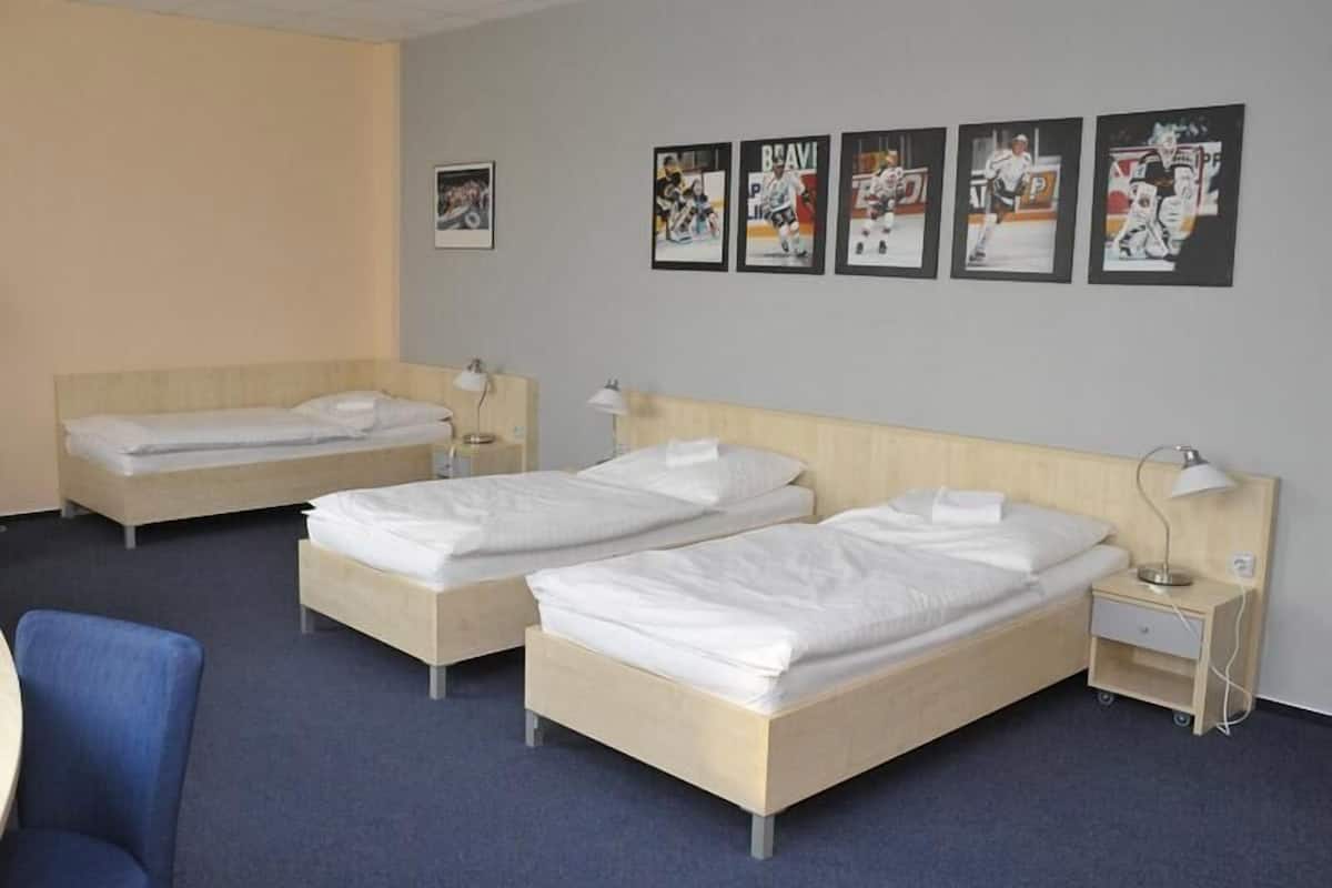 A hotel room with two single beds, a desk, a chair, and a wall with sports-themed posters.