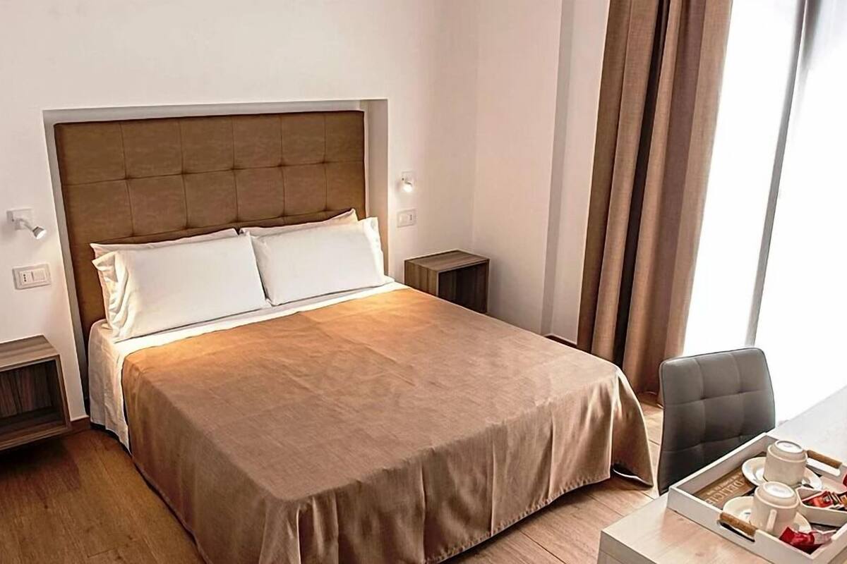 A neatly made bed with a headboard, a bedside table with a lamp, and a tray with cups and snacks.