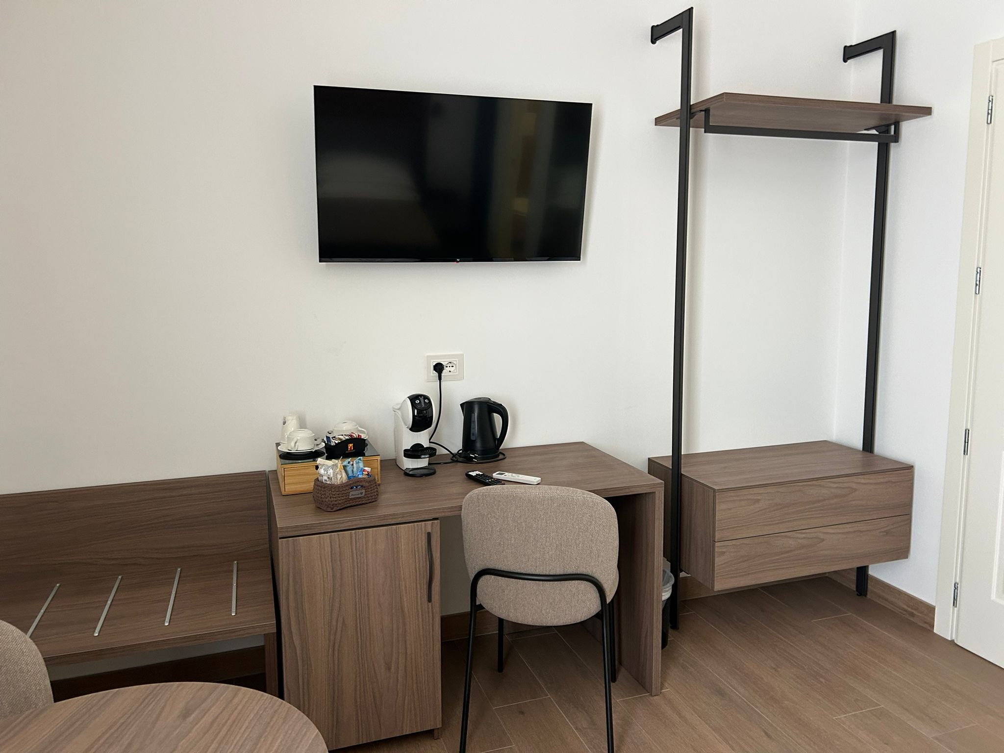 Una camera d'albergo compatta con un letto, una scrivania con sedia, una televisione e una macchina del caffè.