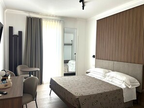 Une chambre d’hôtel équipée d’un lit, d’un bureau, d’une chaise, d’un miroir et d’une fenêtre avec des rideaux.