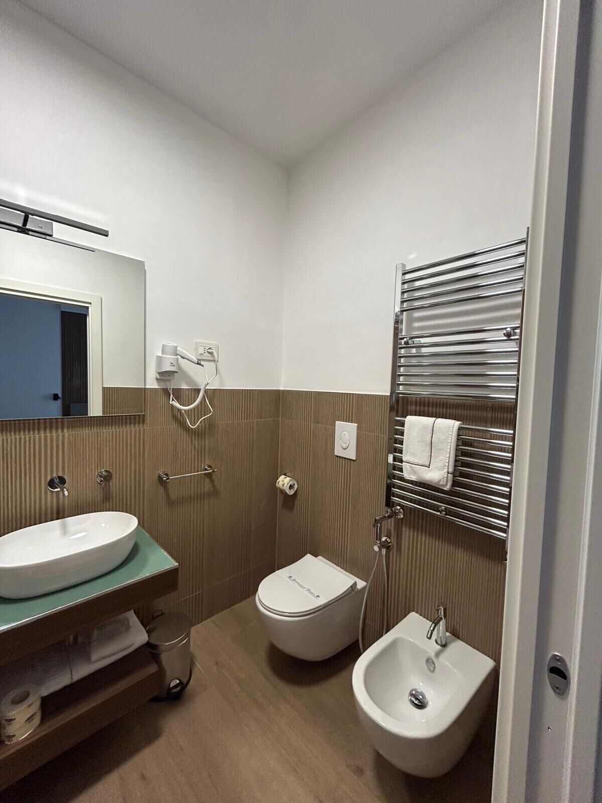 Un baño con lavamanos, bidé, toallero y espejo.