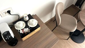 A hotel room with a wooden floor, a black table with a coffee maker, a tray with cups and a candle, and a beige chair. - I Cordari B&B (Vieste)