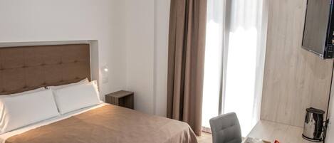 Ein Hotelzimmer mit einem großen Bett, einem Schreibtisch mit Stuhl, einem Fernseher und einer Kaffeemaschine.