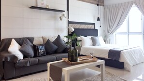 Quarto moderno com sofá cinza, cama com roupa de cama branca, mesa de cabeceira com bandeja e cabeceira de madeira.