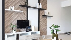 Uma sala de estar moderna com parede de madeira em padrão herringbone, um móvel branco para entretenimento, uma TV de tela plana e objetos decorativos.