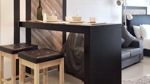 Uma cozinha moderna com ilha central, banquetas de madeira, iluminação pendente e área de refeições com pratos e xícaras brancos.