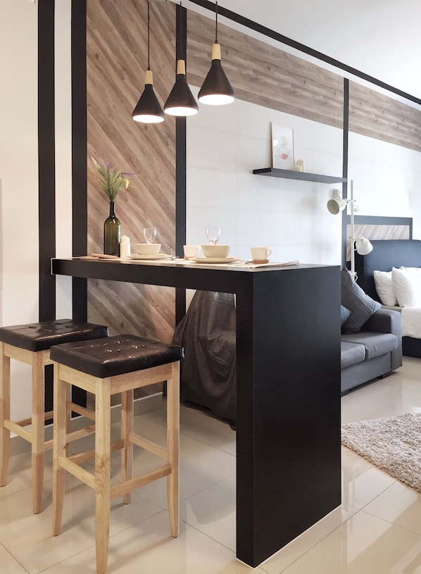 Une cuisine moderne dotée d’un îlot central, de tabourets en bois, de luminaires suspendus et d’un coin repas avec de l’assiette et des tasses blanches.